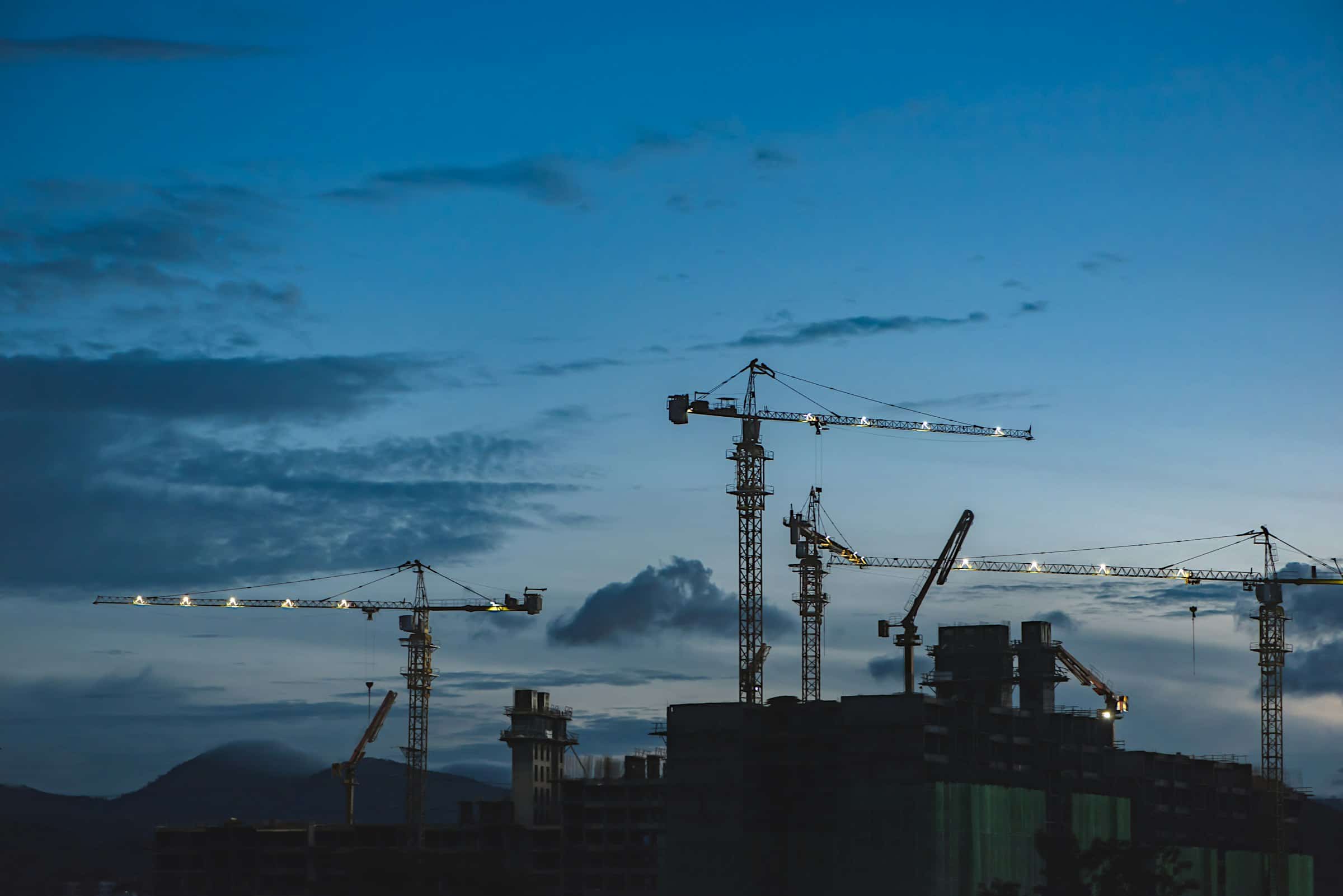 Construction cranes silhouetted against a deep blue dusk sky